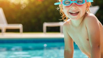 Glatt barn med färgglada simglasögon vid pool