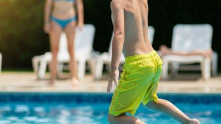 Dreng i badebukser der hopper i pool