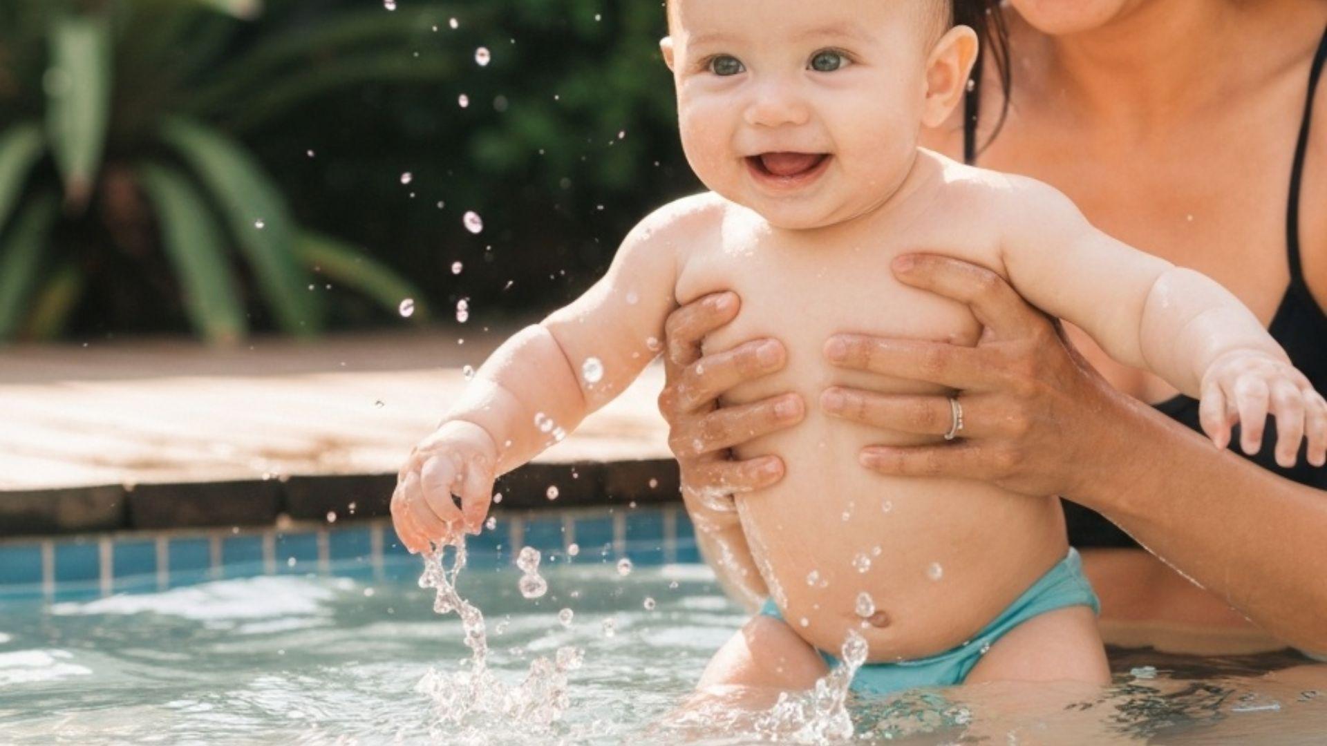 Glad baby som plaskar i barnpool med förälder